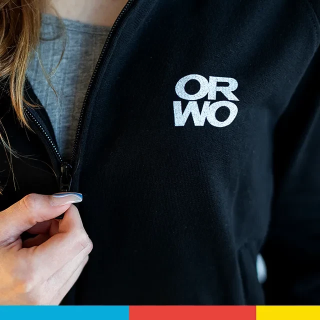 Die ORWO Sweatjacke mit dem kleinen Logo-Print auf der linken Brust ist zu sehen, die gerade von einer Hand via hochwertigen Reißverschluss geöffnet wird.