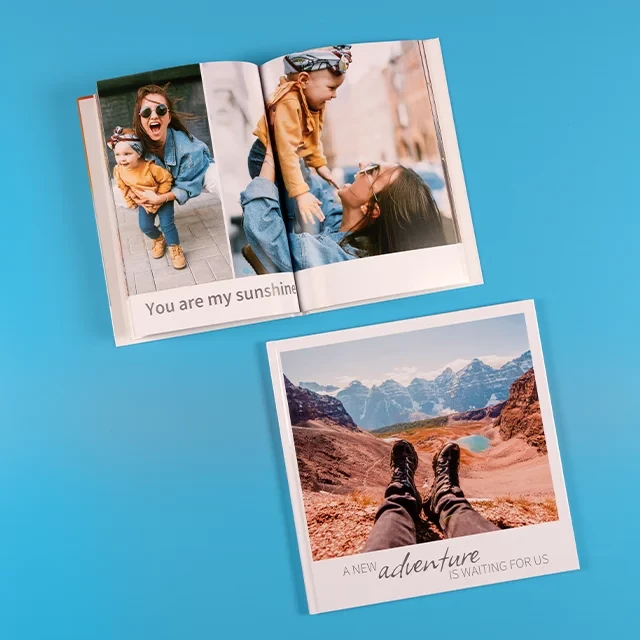 Zwei Fotobücher, ein quadratisches Urlaubs-Fotobuch mit großem Foto und Text und ein aufgeschlagenes, hochformatiges Buch mit Familien-Momenten und passendem Schriftzug.