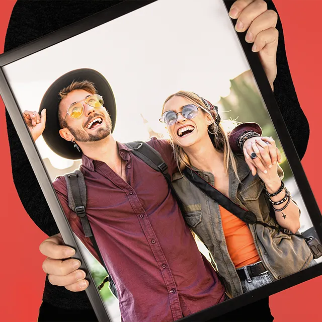 Person hält ein gerahmtes Fotocollage Poster mit lachendem Paar in den Händen vor rotem Hintergrund