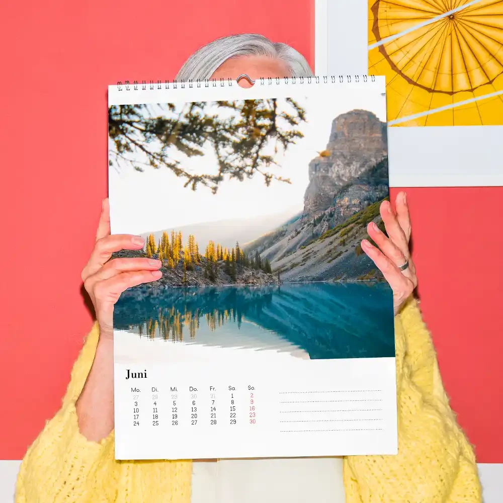 Kalender erstellen, zwischen verschiedenen Varianten wählen Eine ältere Dame hält einen Aktionskalender vor sich, um die herausragende Qualität und die Art und Weise der Bedruckung des günstigen Fotokalenders zu zeigen.