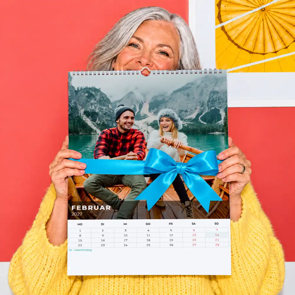Persönlichen Fotokalender verschenken Frau hält einen personalisierten Fotokalender mit einem Paar im Ruderboot und dekorativer Geschenkschleife.