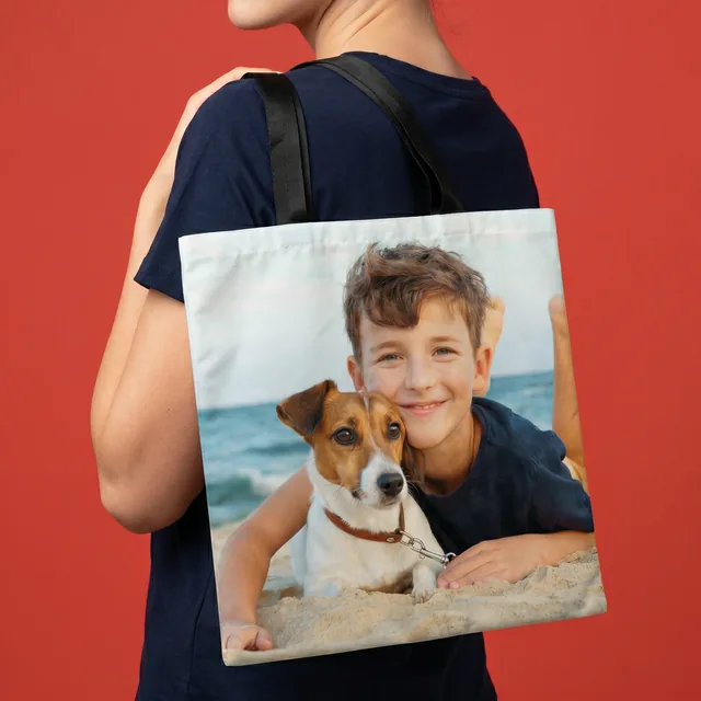 Foto-Stofftasche über der Schulter getragen, vollflächig bedruckt mit dem Foto eines Jungen und seines Hundes am Strand. So wird dein Lieblingsmoment zum Begleiter für unterwegs.