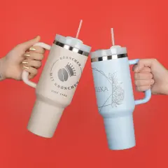 Zwei Stanley ähnliche Thermobecher in den Farben Rosa und Blau mit persönlicher Gravur prosten sich zu. 