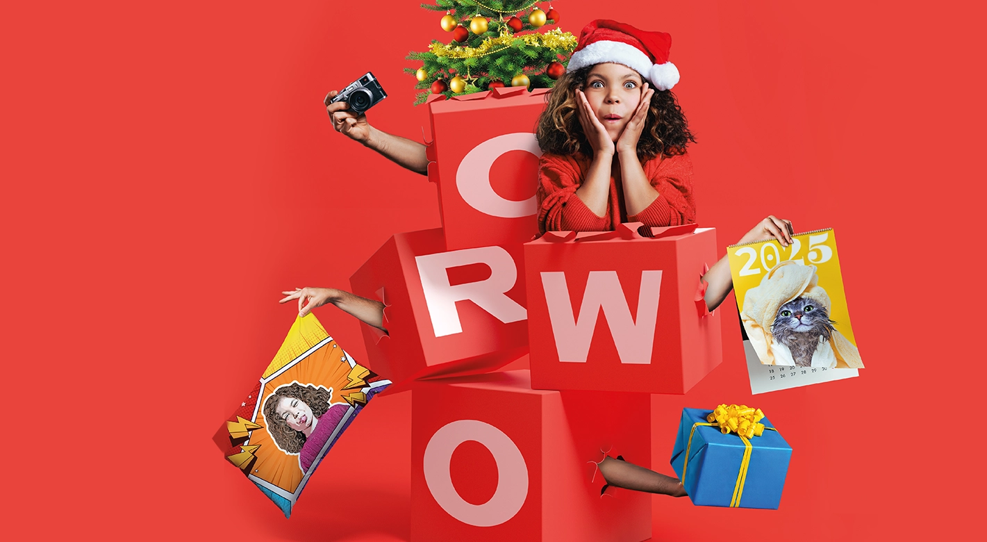 Wild gestapelte Würfel formen das Wort "ORWO" in einer weihnachtlichen Version. Zwischen den Würfeln sind ein geschmückter Tannenbaum, ein kleines Mädchen mit Weihnachtsmütze und staunendem Blick sowie Fotogeschenke Weihnachten zu sehen – eine festliche Inspiration für personalisierte Weihnachtsgeschenke.