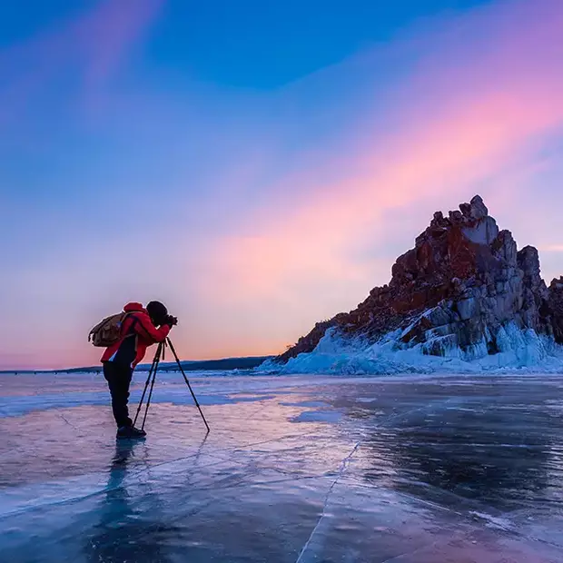 Goldene Stunde am zugefrorenen See: Ein Fotograf mit Stativ fängt die magische Atmosphäre eines im sanften Licht getauchten Steinmassivs ein.