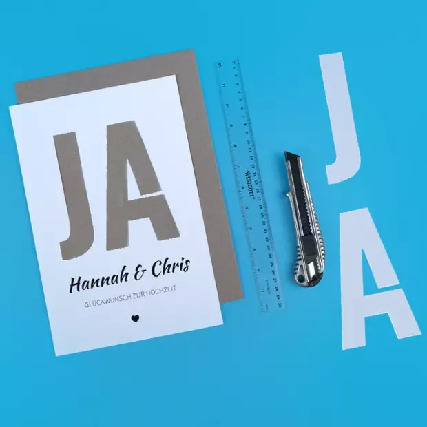 Geldgeschenk verpacken: Sag ja zu dieser Idee Ein Poster mit Hochzeitsdesign, ein Messer und ein Lineal, so einfach kannst du ein Geldgeschenk verpacken.