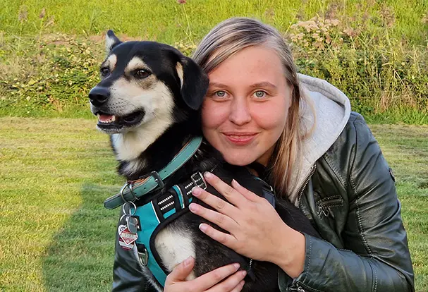 Junge Frau kuschelt lächelnd mit Ihrem Mischlingshund auf einer Wiese. Bei ORWO bekommst du Tipps zur Haustierfotografie!