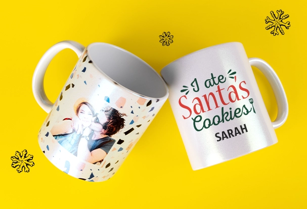 Zwei bedruckte Tassen mit schimmerndem Perlmutteffekt: Eine Tasse zeigt den Aufdruck „I ate Santa’s Cookies. Sarah“, während die andere mit einem bunten Konfettihintergrund und dem Foto eines Pärchens personalisiert ist. Diese Fotogeschenke Weihnachten sind festlich und individuell – perfekt für besondere Momente.