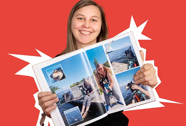 Lachende Frau hält ein Fotobuch mit Urlaubsbildern in die Kamera. Gestalte dein eigenes Hardcover Fotobuch mit ORWO!