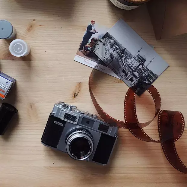 Auf einer Tischfläche liegen eine analoge Kamera, frisch entwickelte Fotoabzüge und ein Negativfilm – klassische Fotografie zum Anfassen.