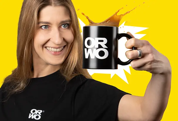 Junge Frau hält lächelnd eine schwarze Tasse mit weißen ORWO Logo in der Hand. Bestelle deine Kaffeetasse bei ORWO.