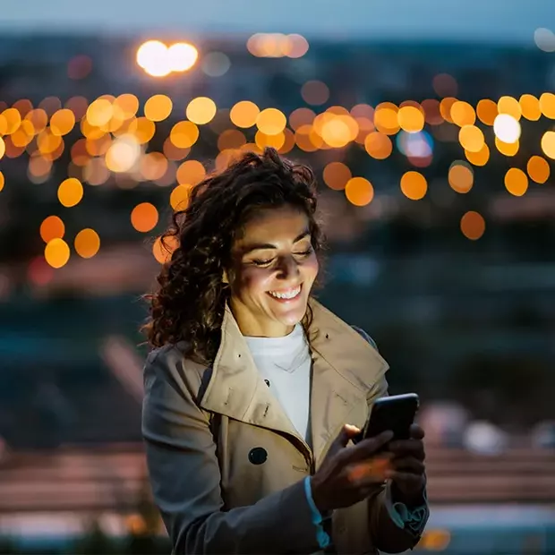 Bokeh-Effekt in den Bergen: Mit den Lichtern der Stadt harmonische Lichtstimmung einfangen Abendstimmung: Ein Smartphone beleuchtet das Gesicht der im Vordergrund stehenden Frau. Dank des Bokeh-Effektes geben die Lichter der Stadt im Hintergrund einen wunderbaren Rahmen.