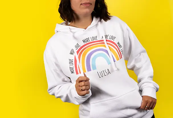 Eine junge Frau im weißen Hoodie mit Regenbogen und ihrem Vornamen. Das neue Produkt steht im Fokus vor neutralem Hintergrund.