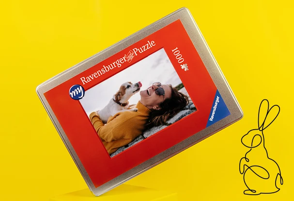 Oster Geschenkideen: Ein personalisiertes Ravensburger Puzzle mit eigenem Foto zeigt eine Frau, die mit ihrem Hund spielt. Verpackt in einer hochwertigen Metallbox.