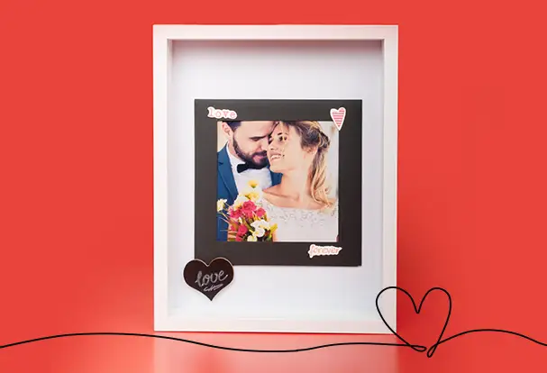 Weiße Magnetrahmenbox mit schwarzem Magnetrahmen und einem Hochzeitsfoto eines jungen Paares, vierziert mit Herzchenstickern. Ein besonders romantisches Geschenk zum Hochzeitstag