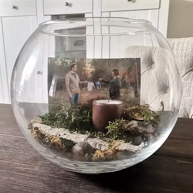 Erinnerungsglas mit Schwangerschaftsfoto Das fertige Erinnerungsglas enthält ein Foto eines Paares, das sich freudig an der Leine mit Babystramplern hält. Es symbolisiert die Vorfreude auf das neue Leben und ist liebevoll im Glas aufbewahrt.