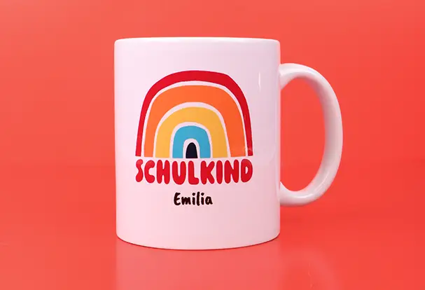 Verschenke zum Schulanfang eine weiße Tasse im bunten „Schulkind“-Design mit Regenbogen. Personalisiere die Tasse mit Namen für noch mehr Individualität.