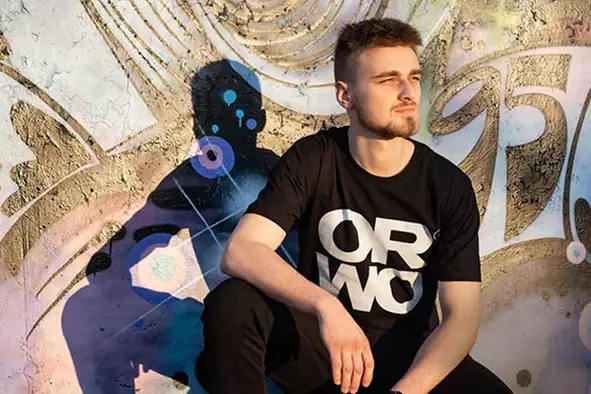 Ein junger Mann präsentiert stolz das neue ORWO Merch aus 2022. Er trägt ein T-Shirt und eine Jogginghose der Marke, die mit dem klassischen ORWO-Logo versehen sind. Dieses Produkt ist ein moderner Ausdruck der ORWO-Historie und verbindet das Erbe der Marke mit frischen, trendigen Designs.
