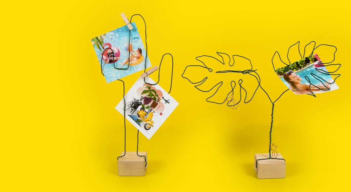 Zwei handgefertigte Fotohalter aus Draht: Einer in Form einer Monstera und der andere als Kaktus. Beide besitzen Standfüße aus Holz und sind kreativ mit persönlichen Fotos dekoriert. Ein einzigartiges DIY-Projekt für individuelle Fotogestaltung.