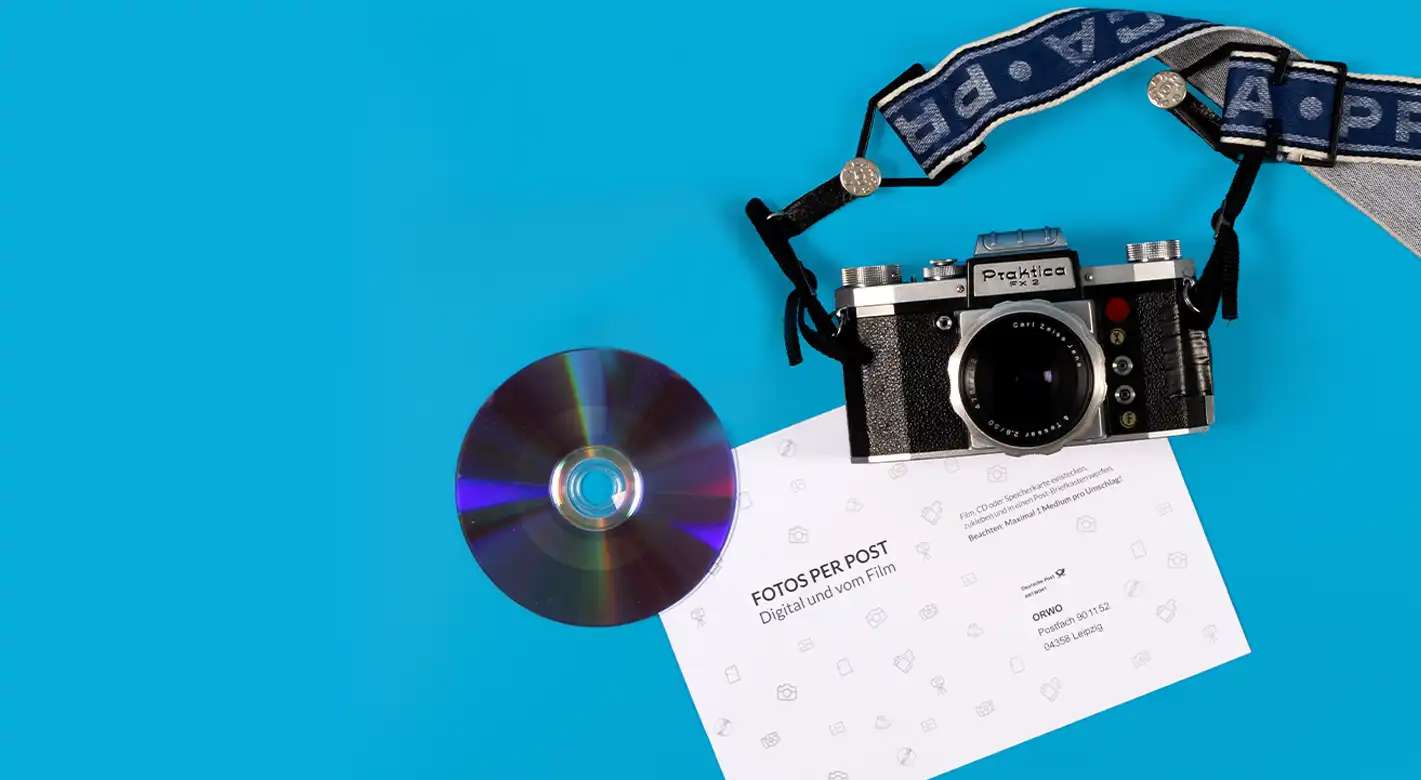 Auf einer Versandtüte liegen eine Kamera, eine CD mit einem personalisierten Aufdruck und ein Bestellformular. Diese Darstellung symbolisiert den Bestellprozess für Produkte per CD bestellen, wobei die CD als Medium dient, um Fotoprodukte zu bestellen.