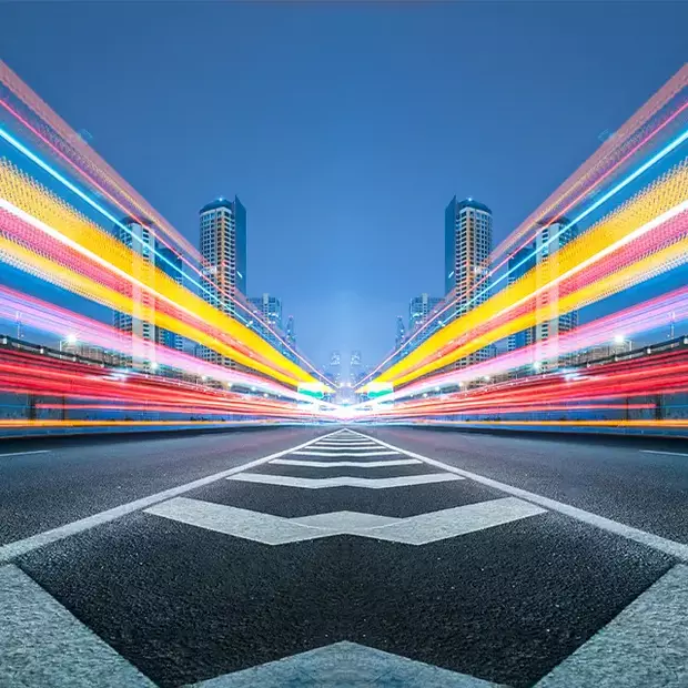 Langzeitbelichtung einer belebten Stadtstraße: Bunte Lichtstreifen, gezeichnet von den sich bewegenden Fahrzeugen, schaffen eine dynamische Nachtszene.