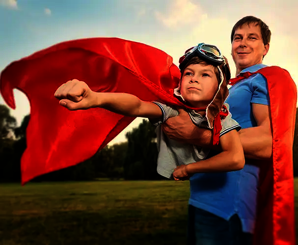Vater und Kind im Superhelden-Outfit mit roten Umhängen im Freien als symbolisches Motiv für starke Familienmomente und persönliche Fotogeschenke zu besonderen Anlässen