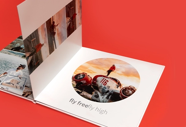 Geöffnetes Reisefotobuch mit Propellerflugzeug und Sonnenuntergang, roter Hintergrund.