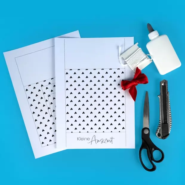 Das benötigst du für dein Tassen Geschenkset: Papier oder Poster, Schere, Kleber, Schleifenband, Locher, Tacker, Fototasse