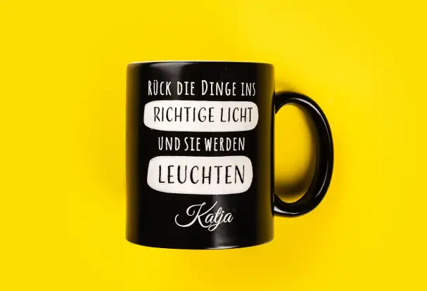 Eine schwarze, seidenmatte Tasse mit dem inspirierenden Spruch „Rück die Dinge ins richtige Licht und sie werden leuchten“, personalisiert mit dem Namen „Katja“. Ein einzigartiges Gravur Geschenk, das täglich Motivation und Freude bringt.