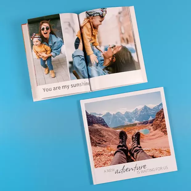 Fotojahrbuch mit Abenteuern und Familienmomenten Quadratisches geschlossenes Buch mit Canyonfoto, daneben geöffnetes Fotobuch mit Familienbildern, blauer Hintergrund.