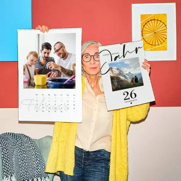 Fotogeschenke Weihnachten – personalisierte Fotokalender mit Lieblingsmomenten Individuelle Fotogeschenke zu Weihnachten – Frau hält zwei personalisierte Fotokalender mit Familienbildern und Reiseerinnerungen in leuchtenden Farben.
