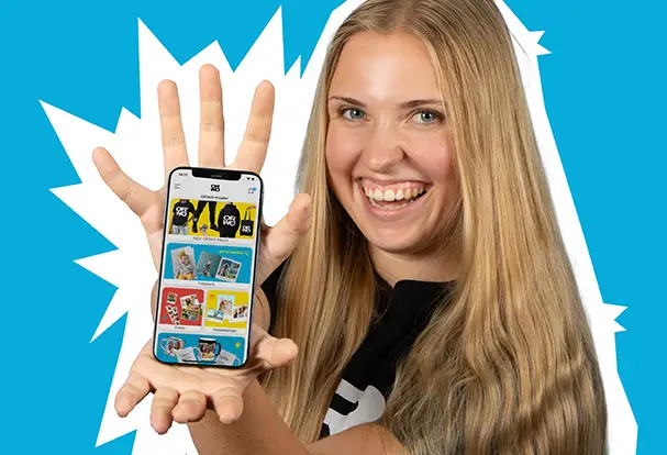 Junge Frau hält lächelnd ihr Smartphone mit der ORWO Foto App vor einem leuchtend blauen Hintergrund. Bestell deine Lieblingsbilder am Handy mit der ORWO FOTO App.