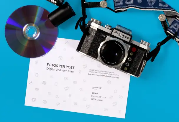 Analoge Filmentwicklung bei ORWO – zu sehen sind eine analoge Kamera, eine CD als Speichermedium und die ORWO-Versandtasche zum Einschicken.