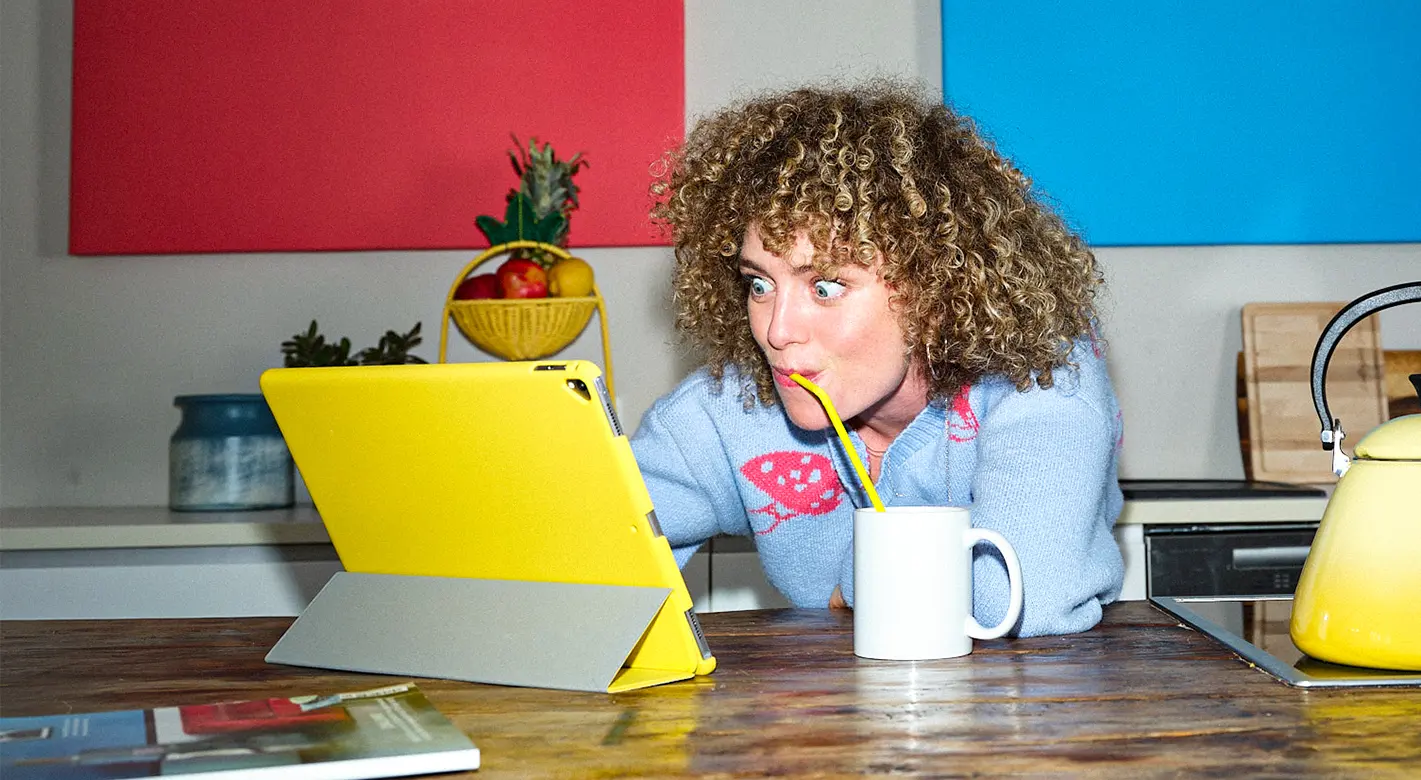 Überraschte Frau sitzt am iPad und entdeckt einzigartige, kreative Foto-Inspirationen von ORWO