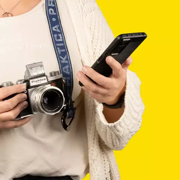 Analogkamera und Smartphone: Informationsaustausch Eine Person informiert sich per Smartphone über die Funktionen ihrer Analogkamera, während sie sie in der Hand hält.
