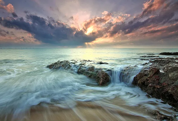 Abendstimmung am Strand mit Felsen und sanft fließendem Wasser. Durch den Einsatz des ND-Filters wirkt das Wasser seidig und elegant, da du eine verlängerte Belichtungszeit an der Kamera einstellen kannst.