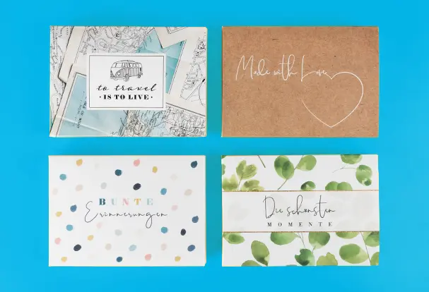 Vier liebevoll gestaltete Bilderboxen für Fotoabzüge mit verschiedenen Designs: Eukalyptus mit „Die schönsten Momente“, Konfetti mit „Bunte Erinnerungen“, braunes Kraftpapier mit „Made with Love“ und Landkarten mit „To travel is to live“. Diese Boxen sind eine stilvolle Möglichkeit, die Erinnerungen an den Hochzeitstag aufzubewahren.