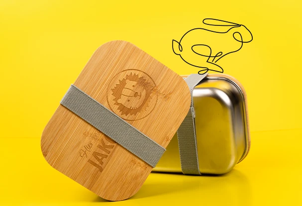 Oster Geschenkideen: Eine stilvolle Metall-Lunchbox mit einem gravierten Holzdeckel. Die Gravur zeigt den Namen Lukas und einen Löwenkopf.