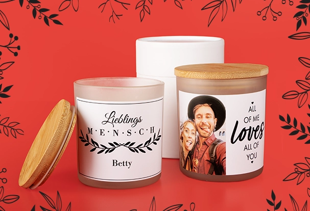 Zwei stilvolle Duftkerzen im Glas mit Holzdeckel und individuell bedrucktem Etikett: Ein Design trägt die Aufschrift „Lieblingsmensch“, das andere zeigt „All of me loves all of you“ mit einem romantischen Bild eines Paares. Diese Fotogeschenke Weihnachten verbinden persönliche Botschaften mit gemütlichem Flair.