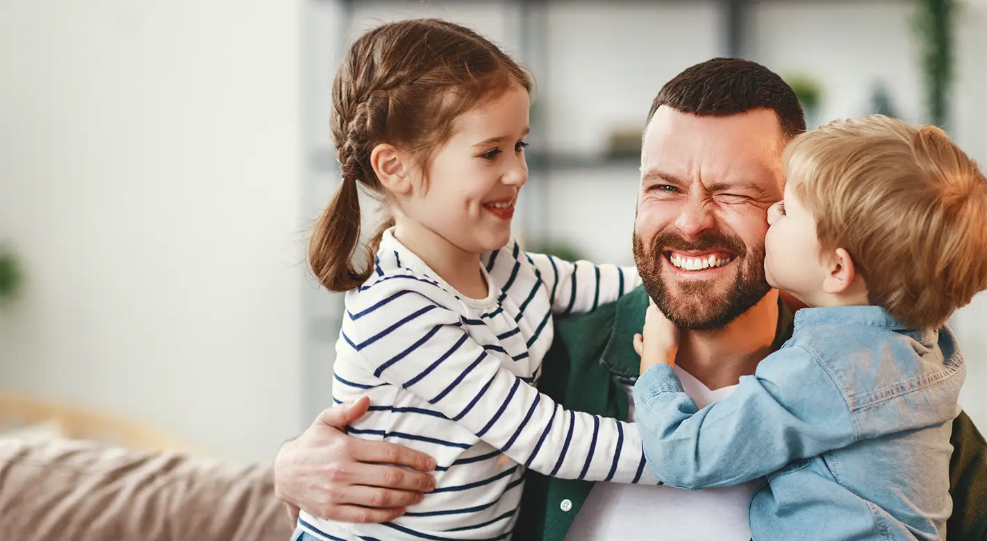 Strahlender Vater wird von seinen beiden Kindern umarmt und geküsst – liebevolle Fotoidee Vatertag.