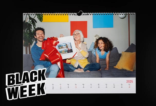 Individueller Fotokalender für das Jahr 2026 mit fröhlicher Familie auf dem Sofa, dekoriert mit großer roter Schleife, beworben als Black-Week-Sonderangebot.
