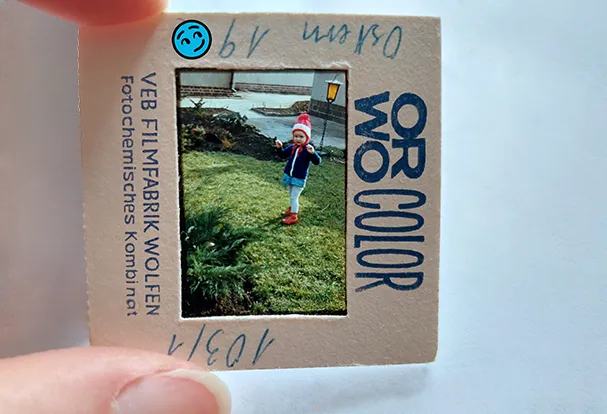 Tipps zur Analogfotografie gibt's von ORWO Zwischen Daumen und Zeigefinger gehaltenes altes ORWO-Farbdia mit einem Kind auf einer Wiese. Entdecke ORWOs Analogwelt.