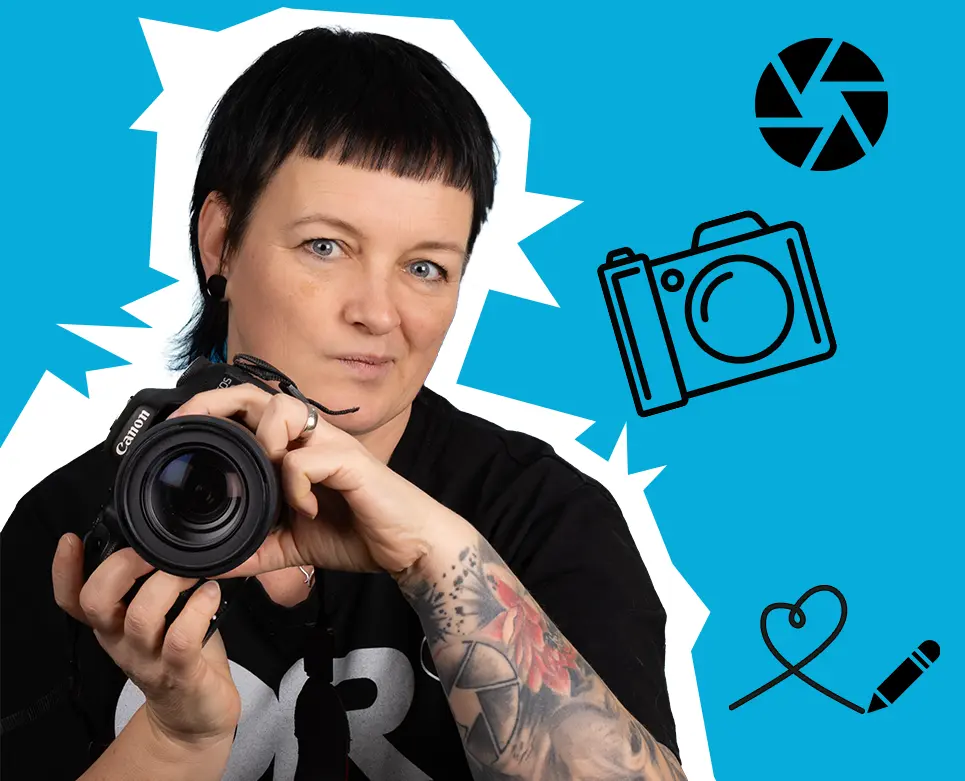 Katja – ORWOs kreatives Multitalent Tätowierte Fotografin hält eine Kamera vor blauem Hintergrund mit Kamera-Icons. Mach mehr aus deinen Fotos. Mach ORWO!
