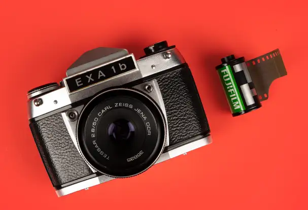 Eine gut erhaltene analoge Spiegelreflexkamera neben einem Fuji Kleinbildfilm, bereit für kreative Aufnahmen.
