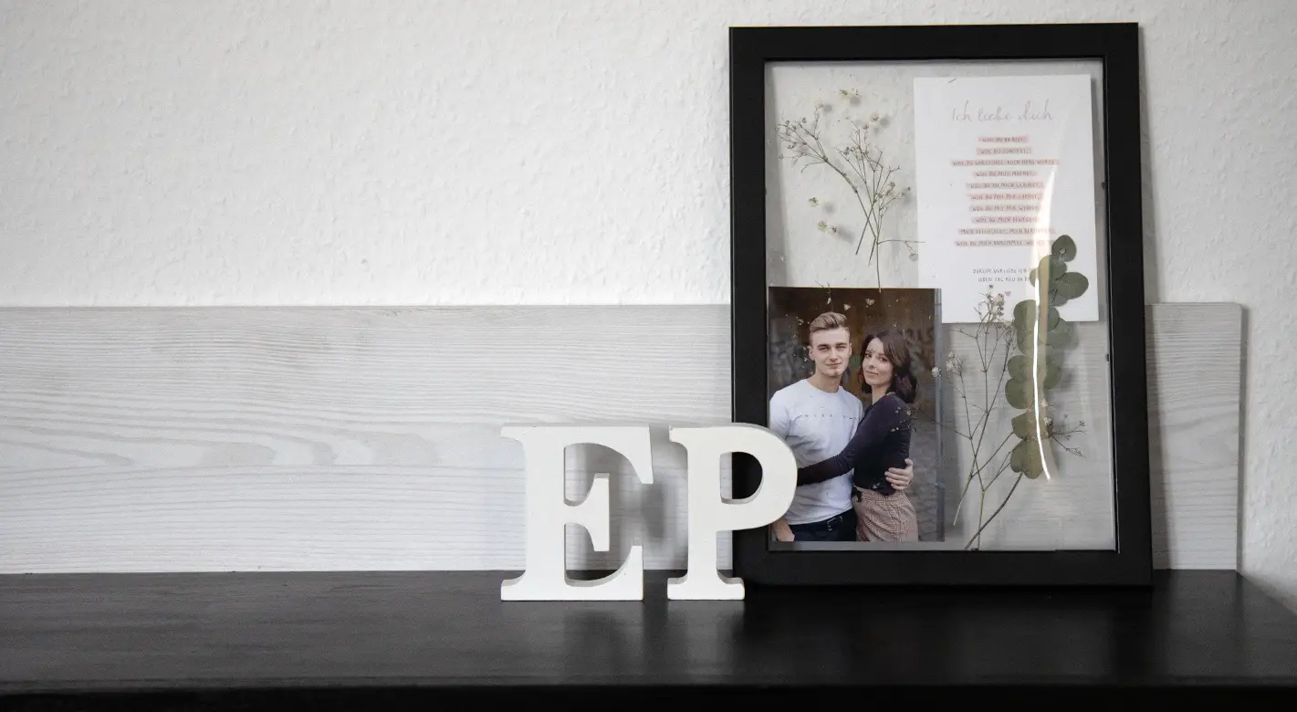 Bilderrahmen einmal anders: Ersetze die Rückwand aus Pappe mit einer weiteren Glasscheibe. Ein DIY Bilderrahmen mit zwei Glasscheiben, ohne traditionelle Rückwand. Zwischen diesen Glasscheiben sind ein Foto, ein geschriebener Text und Trockenblumen zu sehen.