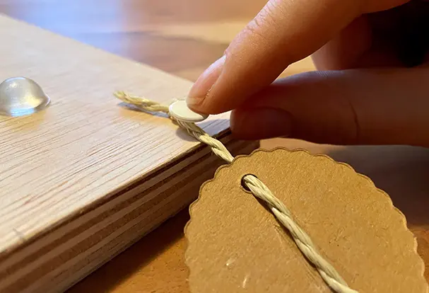 Auf der Rückseite des Geburtstagskalenders aus Holz sind die personalisierten Pappschilder bereits mit Hilfe von Reißzwecken an der Schnur befestigt. So wird die Schnur sicher gehalten, um die Namen der Geburtstagskinder anzuzeigen. Ein weiterer Schritt auf dem Weg zu deinem einzigartigen DIY-Kalender!