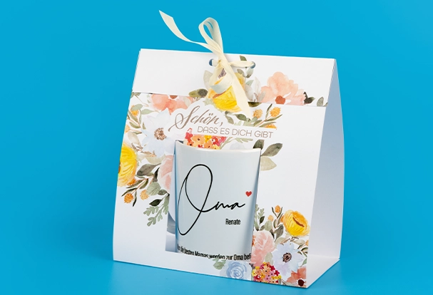 Kalender mit Kinderbildern: Kreative Geschenkverpackung für Tassen Eine individuell bedruckte Fototasse, liebevoll verpackt in einer Papierhülle mit buntem Motiv. Diese kreative Verpackungsidee passt perfekt zu einem Kalender mit Kinderbildern als persönliches Geschenk.