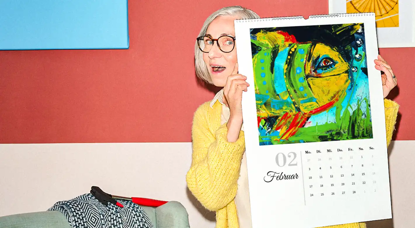 Kalender mit Kinderbildern: Freude über kreativen Wandschmuck Eine ältere Frau präsentiert freudig einen großen Kalender. Neben dem Kalendarium und Monatsnamen ist ein kunterbuntes, gemaltes Bild eines Fisches zu sehen.