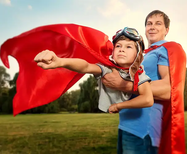 Starke Familienmomente verschenken Vater und Kind im Superhelden-Outfit mit roten Umhängen im Freien als symbolisches Motiv für starke Familienmomente und persönliche Fotogeschenke zu besonderen Anlässen
