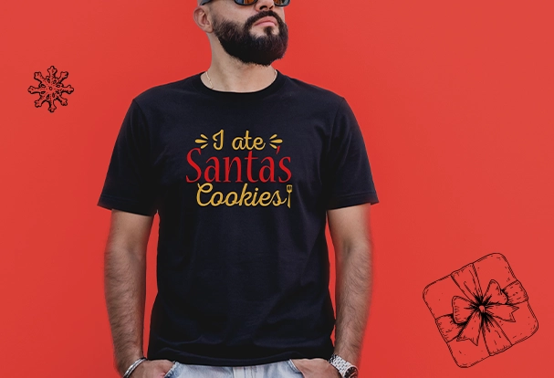Personalisierte Weihnachtsgeschenke: T-Shirt mit individueller Botschaft Ein Mann trägt ein schwarzes T-Shirt, das mit seinem Namen und dem humorvollen Spruch „I ate Santa’s Cookies“ bedruckt ist. Dieses personalisierte Fotogeschenk Weihnachten bringt einen lustigen Akzent in die festliche Saison und ist ein tolles Geschenk für die besonderen Menschen.